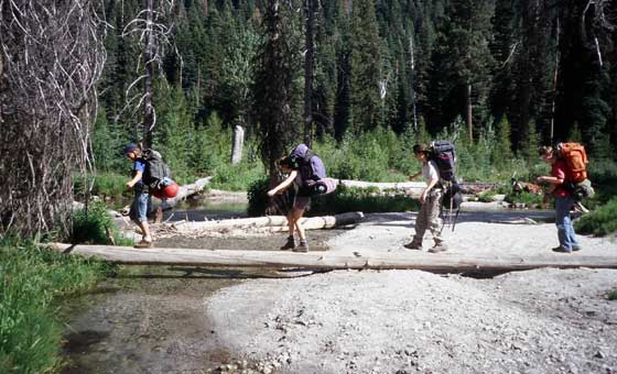 String of backpackers crossing a creek on a log